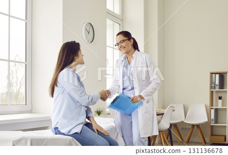 Friendly doctor shaking hands with a young patient woman in medical clinic after exam. 131136678
