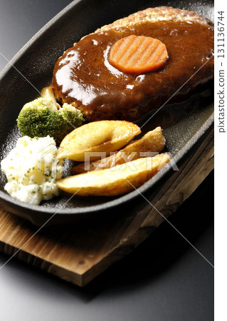 Hamburger steak plate with side dishes of fries, potato salad, and broccoli photographed against a black background Hamburger steak plate with side dishes of fries, potato salad, and broccoli photographed against a black background 131136744