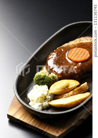 Hamburger steak plate with side dishes of fries, potato salad, and broccoli photographed against a black background Hamburger steak plate with side dishes of fries, potato salad, and broccoli photographed against a black background 131136745