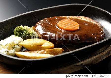 Hamburger steak plate with side dishes of fries, potato salad, and broccoli photographed against a black background 131136763