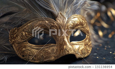 Elegant gold masquerade mask with intricate designs and feathers, set against dark background 131136954
