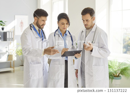 Three medical professionals share ideas and discuss patient care strategies while working in clinic. Three medical professionals share ideas and discuss patient care strategies while working in clinic. 131137222