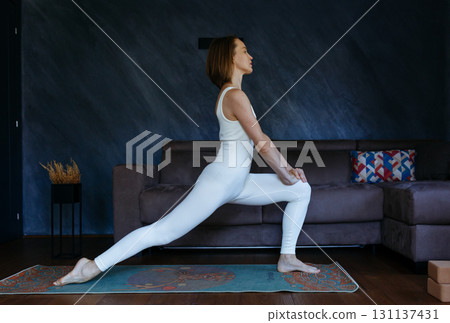 woman practicing yoga standing in Crescent Lunge pose at home woman practicing yoga standing in Crescent Lunge pose at home 131137431