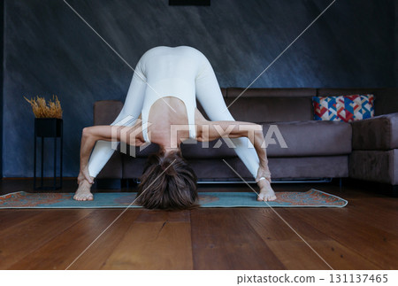 front view of a woman standing in Wide Legged Forward Bend yoga pose at home front view of a woman standing in Wide Legged Forward Bend yoga pose at home 131137465