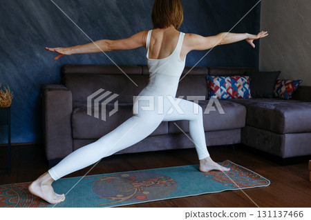 woman practicing yoga standing in Warrior I pose at home woman practicing yoga standing in Warrior I pose at home 131137466