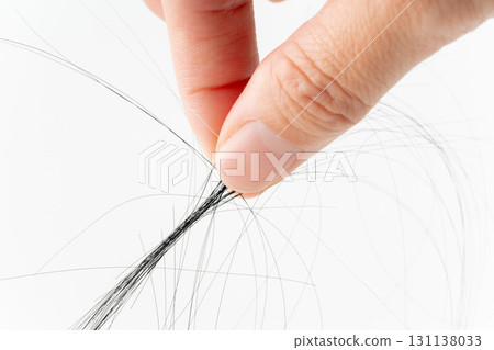 Close-up of hair pinched between fingers on white background 131138033