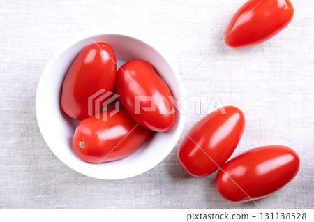 Fresh plum tomatoes, Roma tomatoes in a white bowl, on linen. Also known as processing or paste tomatoes, oval shaped, used for canning or producing tomato paste, because of its slender, firm nature. 131138328