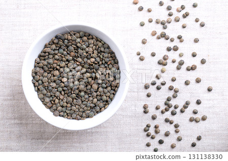 Puy lentils in a white bowl on linen. Dried variety of small lentils, mottled, of slate-gray to dark green color, with blue marbling. Lens esculenta variety, grown in the Auvergne region of France. Puy lentils in a white bowl on linen. Dried variety of small lentils, mottled, of slate-gray to dark green color, with blue marbling. Lens esculenta variety, grown in the Auvergne region of France. 131138330