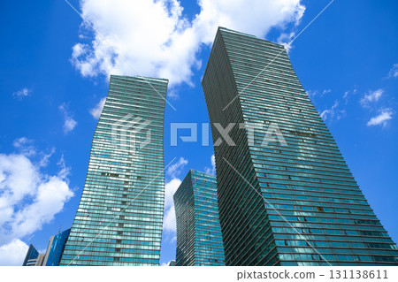 Modern glass towers surrounded by trees under a bright blue sky in an urban environment, view from below from street. improvement, beautification, renovation Modern glass towers surrounded by trees under a bright blue sky in an urban environment, view from below from street. improvement, beautification, renovation 131138611