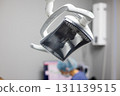 Bright dental light hangs above, casting a warm glow as a dentist tends to a patient's needs. The room is equipped with advanced technology, creating a welcoming environment. 131139515