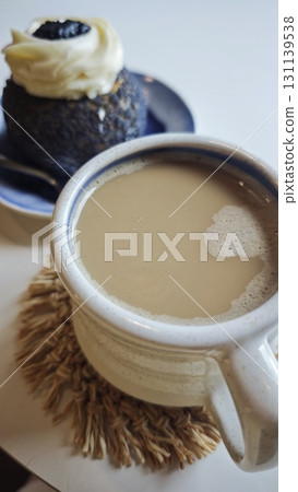 A ceramic cup of coffee with milk served next to a dessert topped with cream on a plate 131139538