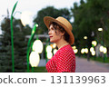 Side portrait of woman in red dress and straw hat at dusk. 131139963