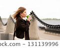 Young woman holding coffee cup looking into distance in outdoor urban setting. 131139996