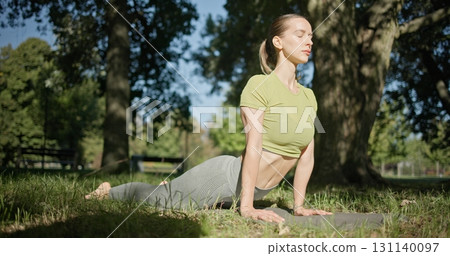 young beautiful white girl doing yoga in park among trees in clearing on summer day 131140097
