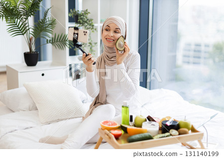 Young Muslim woman wearing hijab records skincare tips using avocado in bright modern room 131140199
