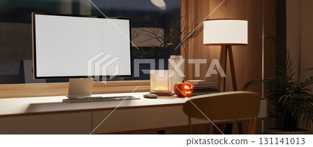 Blank screen laptop and glowing halloween pumpkin on wooden table aside lamp and window dim lit room 131141013