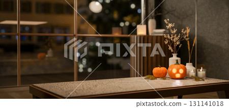 Glowing jack-o-lantern halloween pumpkin and candles on marble table aside glass wall in living room 131141018