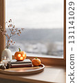 Glowing jack-o-lantern halloween pumpkin on books and candles in tray over wooden table aside window 131141029