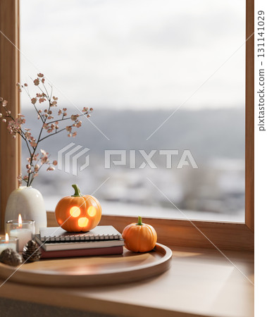 Glowing jack-o-lantern halloween pumpkin on books and candles in tray over wooden table aside window 131141029