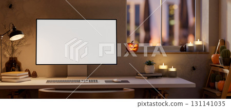 White screen computer on table with halloween pumpkin lanterns and candles on window in dim lit room 131141035