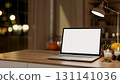 White screen laptop with pumpkin and aroma scented candle aside lamp on wooden table in dim lit room 131141036