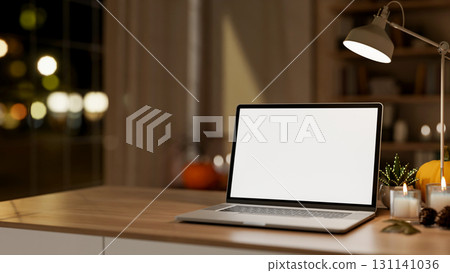 White screen laptop with pumpkin and aroma scented candle aside lamp on wooden table in dim lit room 131141036