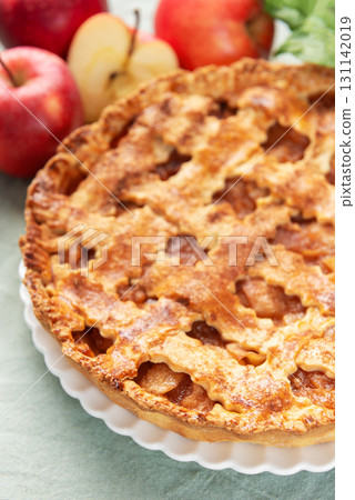 Freshly baked apple pie with red apples and leaves on green tablecloth Freshly baked apple pie with red apples and leaves on green tablecloth 131142019