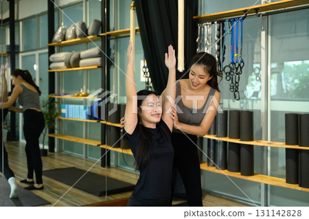 Female coach guiding student in mindful practice, encouraging balance and proper form in yoga session 131142828