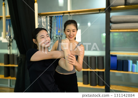 Female trainer guiding teenage girl through an arm stretch exercise in a fitness studio Female trainer guiding teenage girl through an arm stretch exercise in a fitness studio 131142884
