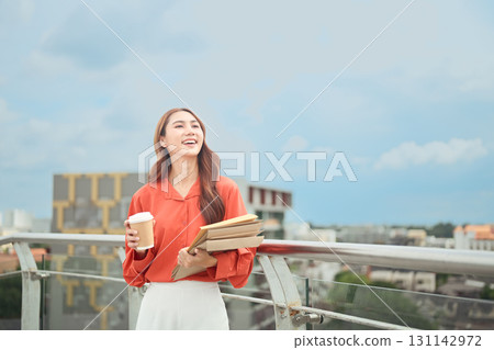 Happy businesswoman enjoying coffee break while standing on rooftop with city skyline Happy businesswoman enjoying coffee break while standing on rooftop with city skyline 131142972
