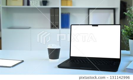 Modern workspace with a laptop, coffee cup, and tablet on a clean white desk Modern workspace with a laptop, coffee cup, and tablet on a clean white desk 131142996