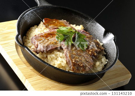 Garlic rice topped with grilled meat photographed against a black background 131143210