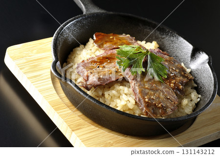 Garlic rice topped with grilled meat photographed against a black background 131143212