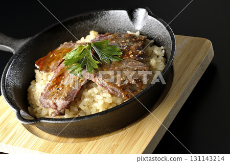 Garlic rice topped with grilled meat photographed against a black background 131143214