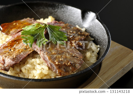 Garlic rice topped with grilled meat photographed against a black background Garlic rice topped with grilled meat photographed against a black background 131143218