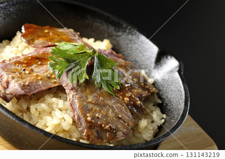 Garlic rice topped with grilled meat photographed against a black background Garlic rice topped with grilled meat photographed against a black background 131143219