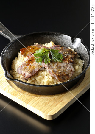Garlic rice topped with grilled meat photographed against a black background 131143223