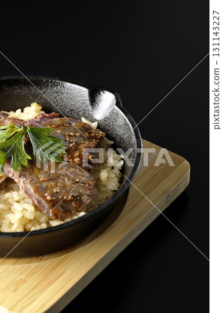 Garlic rice topped with grilled meat photographed against a black background 131143227