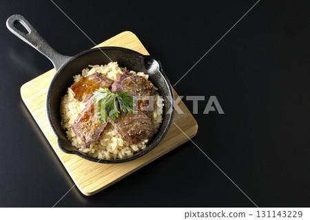 Garlic rice topped with grilled meat photographed against a black background 131143229