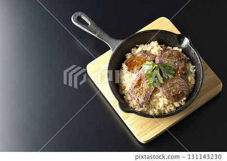 Garlic rice topped with grilled meat photographed against a black background Garlic rice topped with grilled meat photographed against a black background 131143230