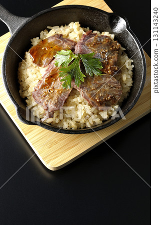 Garlic rice topped with grilled meat photographed against a black background Garlic rice topped with grilled meat photographed against a black background 131143240