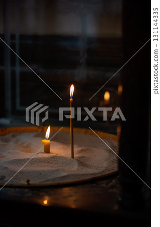 Lit church candles in sand tray, symbolic prayer and remembrance in dim sacred space Lit church candles in sand tray, symbolic prayer and remembrance in dim sacred space 131144335