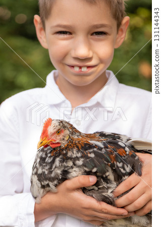 Smiling boy holding chicken outdoors in summer garden 131144343