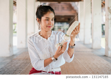 A woman in traditional Thai attire holds a floral garland, showcasing cultural heritage and intricate architecture. A woman in traditional Thai attire holds a floral garland, showcasing cultural heritage and intricate architecture. 131147185