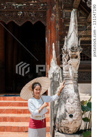A woman holding a parasol stands beside a detailed stone sculpture at a historic temple, showcasing traditional architecture. 131147190