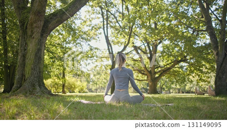 A young beautiful white girl practices yoga in the park and meditates in the lotus position among the trees in a clearing on a summer day A young beautiful white girl practices yoga in the park and meditates in the lotus position among the trees in a clearing on a summer day 131149095