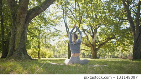 A young beautiful white girl practices yoga in the park and meditates in the lotus position among the trees in a clearing on a summer day A young beautiful white girl practices yoga in the park and meditates in the lotus position among the trees in a clearing on a summer day 131149097