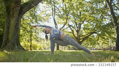 young beautiful white girl doing yoga in park among trees in clearing on summer day 131149157