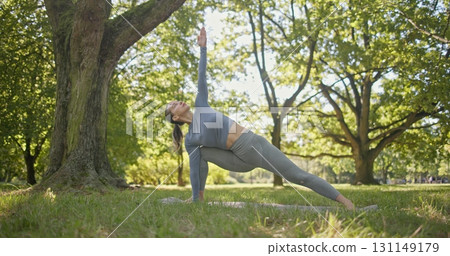 young beautiful white girl doing yoga in park among trees in clearing on summer day 131149179