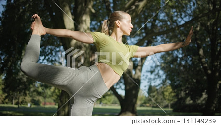 young beautiful white girl doing yoga in park among trees in clearing on summer day 131149239